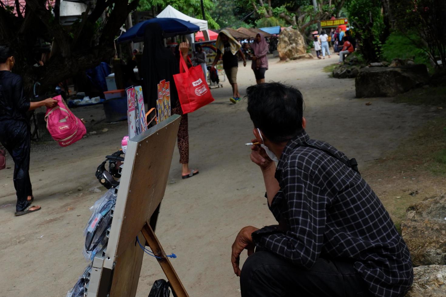 lampung, indonésia - 6 de maio de 2022, um vendedor de brinquedos está de cócoras enquanto fuma no mercado foto