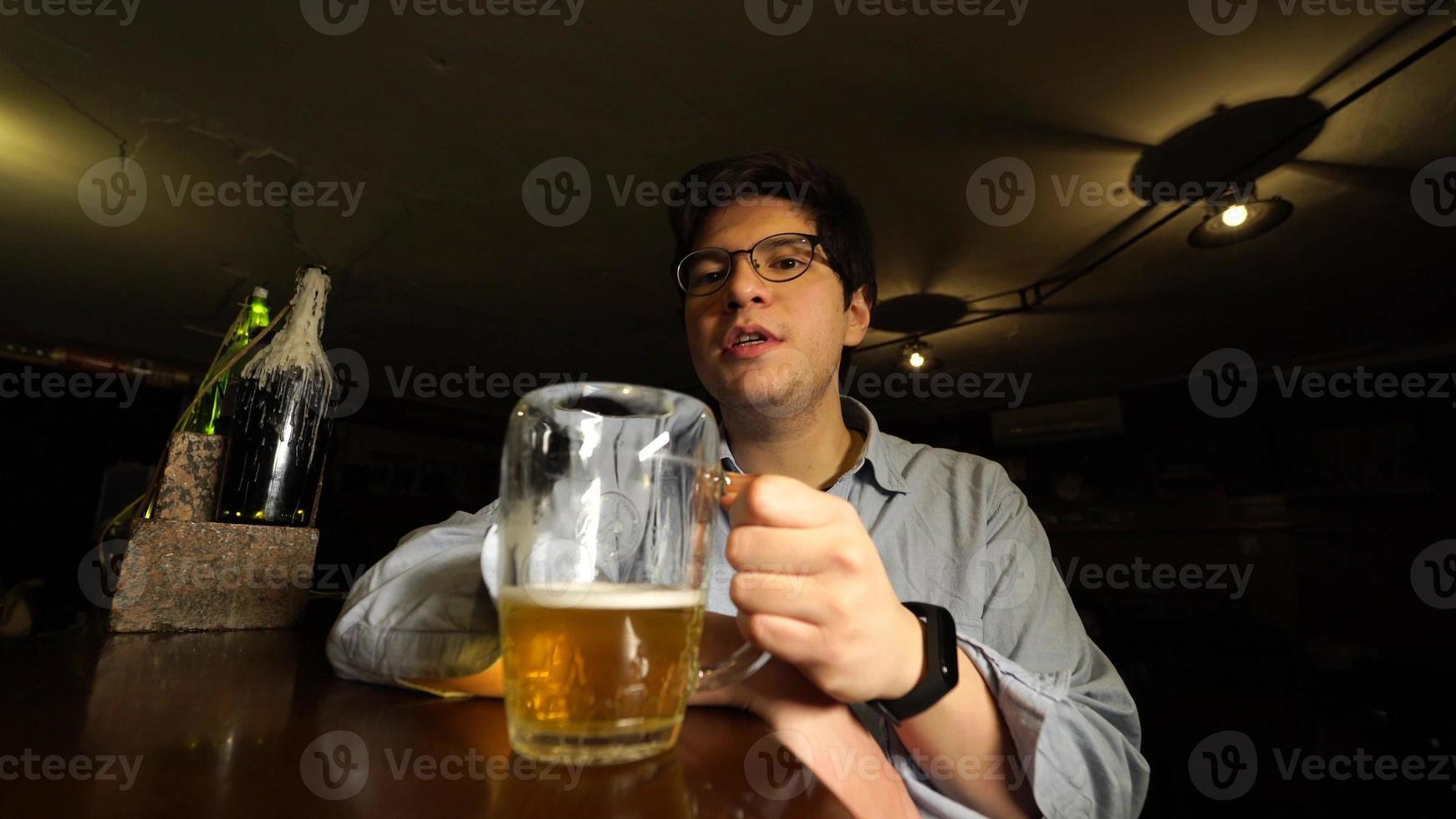 cara bebendo cerveja e conversando com a câmera no bar à noite foto