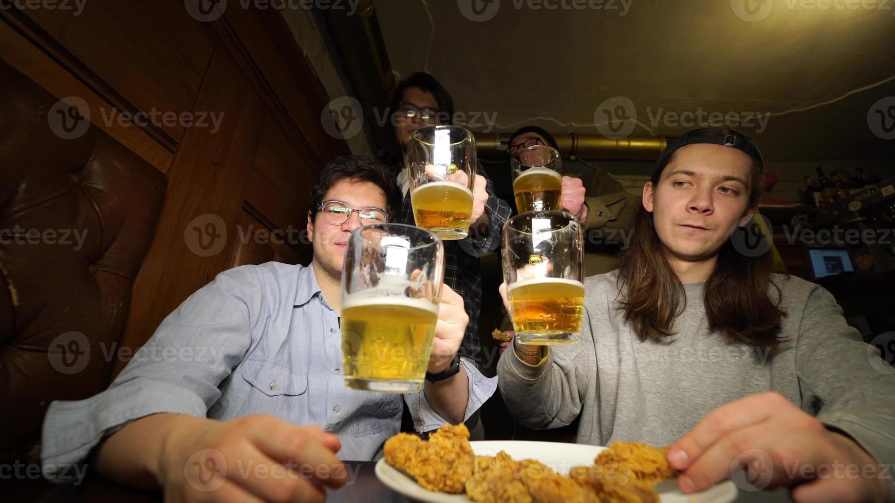 jovens amigos se divertindo juntos bebendo cerveja e tilintando copos em um pub. foto