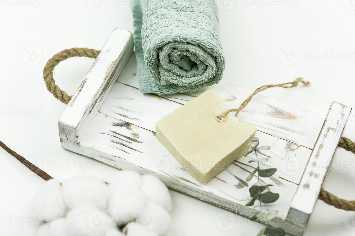 um sabonete branco, um ramo de eucalipto e uma toalha de algodão para spa estão em uma bandeja de madeira branca. conceito positivo do corpo foto