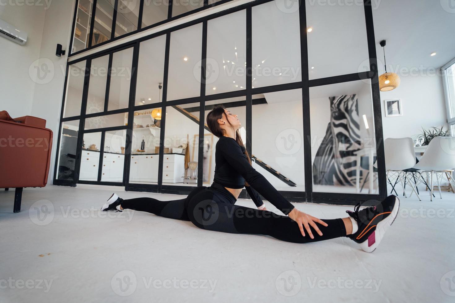 jovem fêmea vestindo terno esportivo preto exercitando pose de ioga dentro de casa. foto
