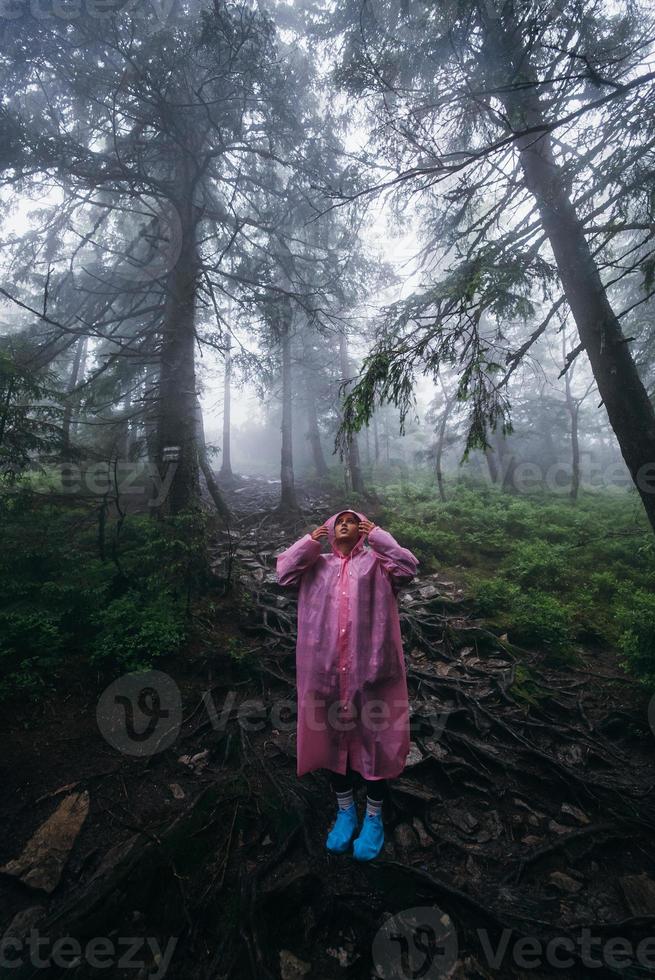 jovem em uma capa de chuva caminha pela floresta na chuva foto