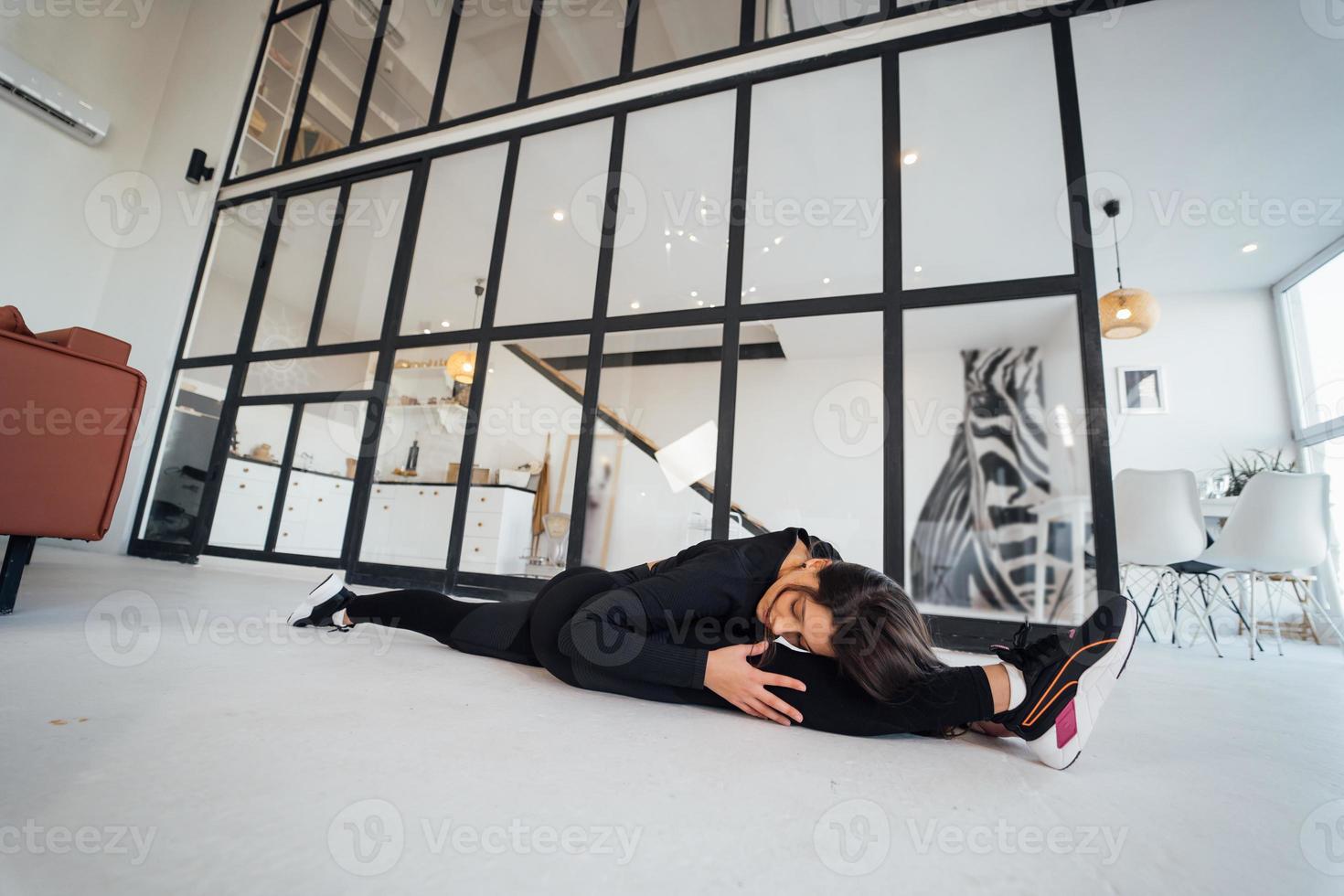 jovem fêmea vestindo terno esportivo preto exercitando pose de ioga dentro de casa. foto