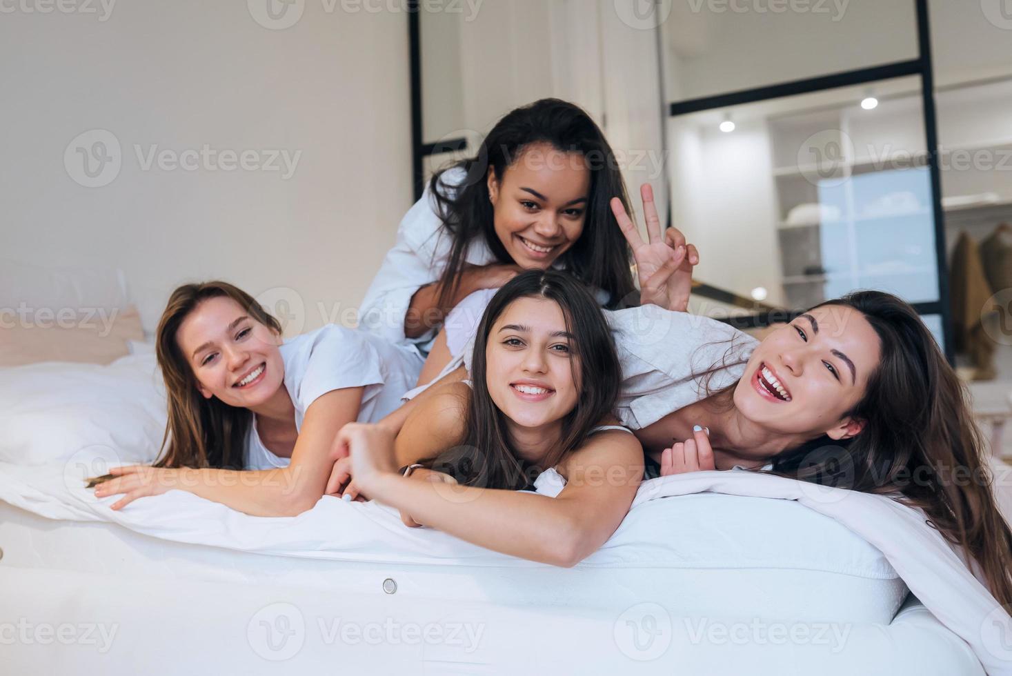 meninas positivas mulheres amigas dentro de casa na cama na festa de despedida em casa. foto