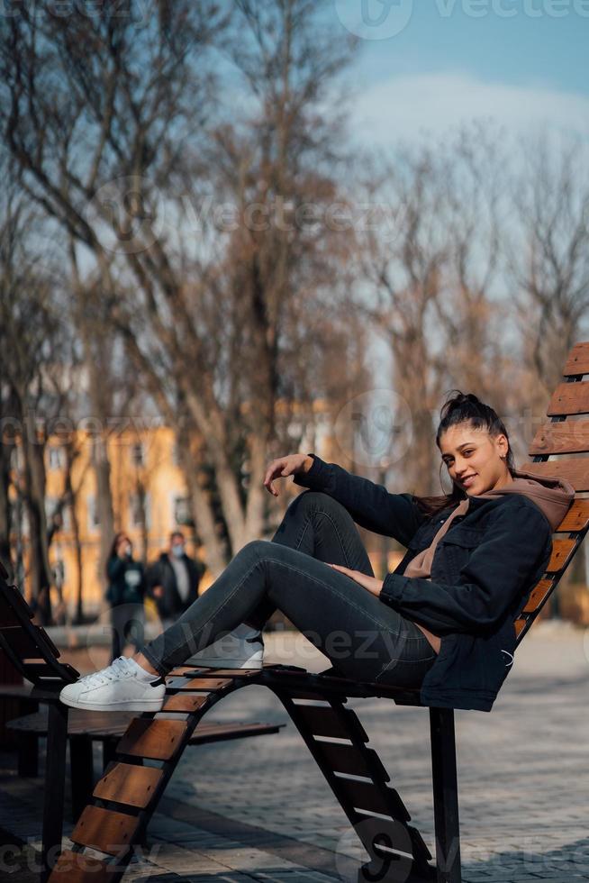 jovem sentada no banco no parque, sorrindo e olhando para a câmera foto