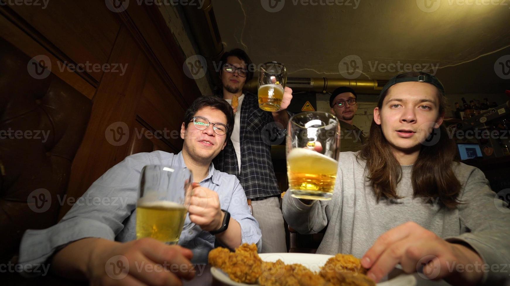 jovens amigos se divertindo juntos bebendo cerveja e tilintando copos em um pub. foto