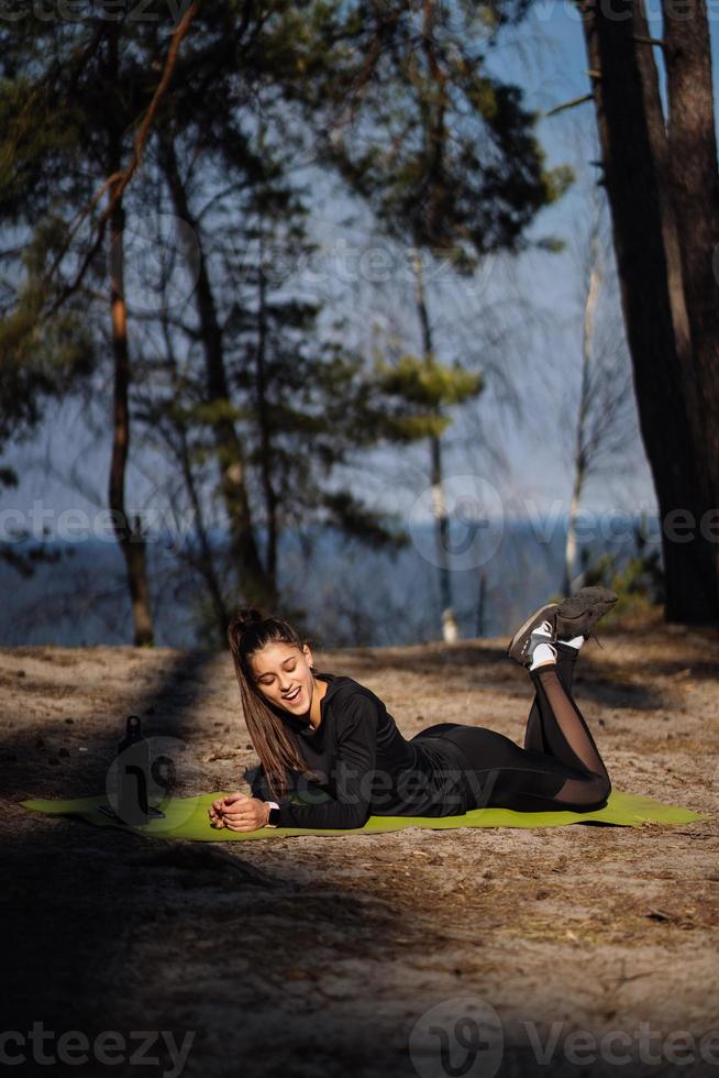 linda garota de roupas esportivas deitada em uma esteira no parque. foto