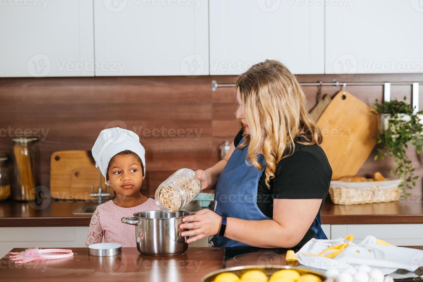 mãe e filha despejam aveia em uma tigela na cozinha foto