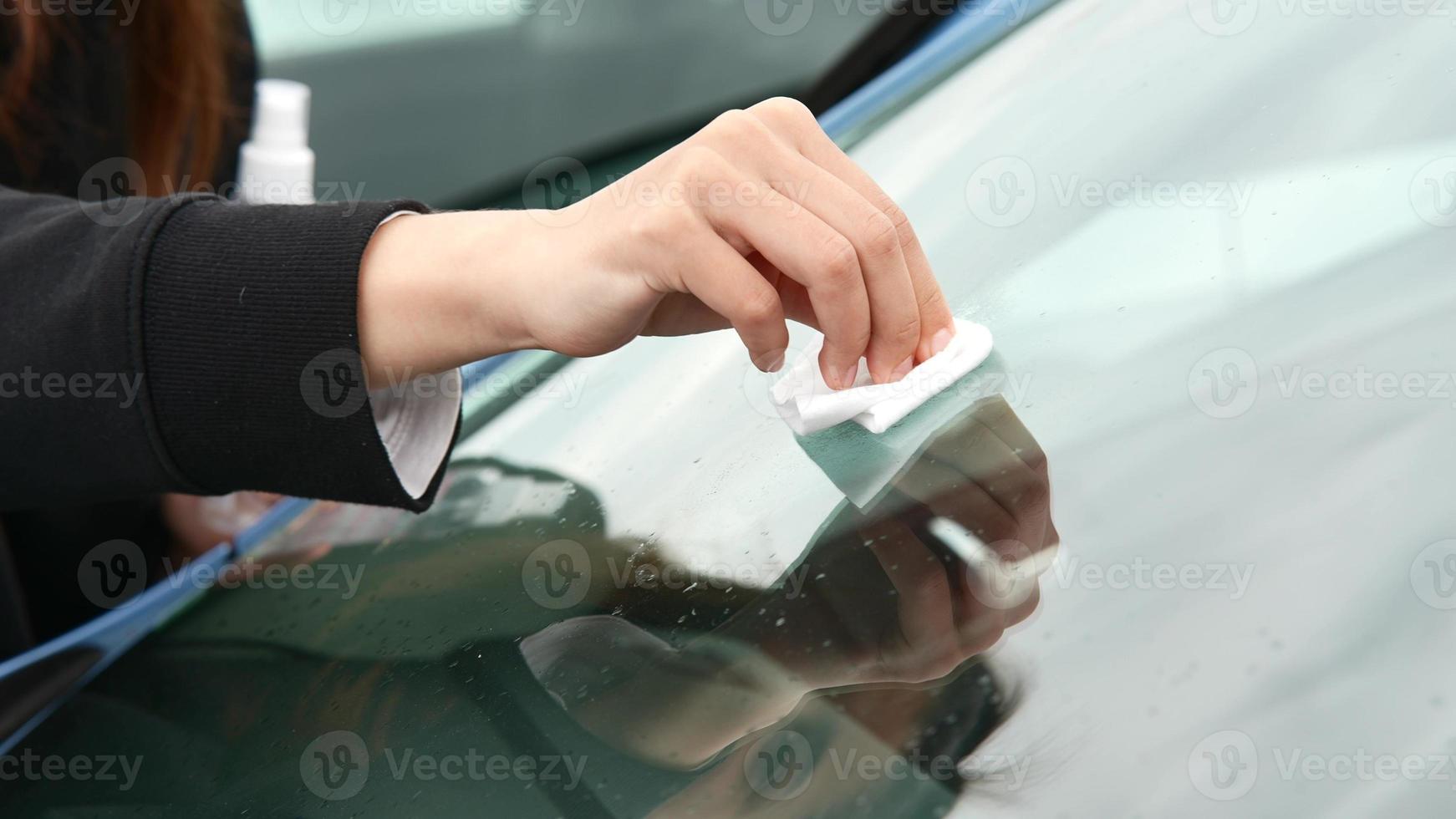 garota pulverizando detergente de limpeza e limpe a janela do carro. foto