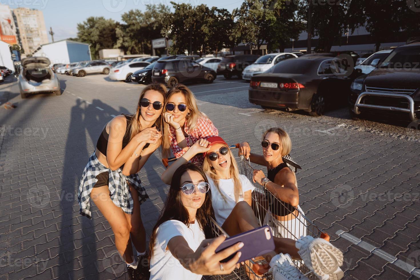 cinco meninas se divertem com um carrinho de supermercado em um estacionamento foto