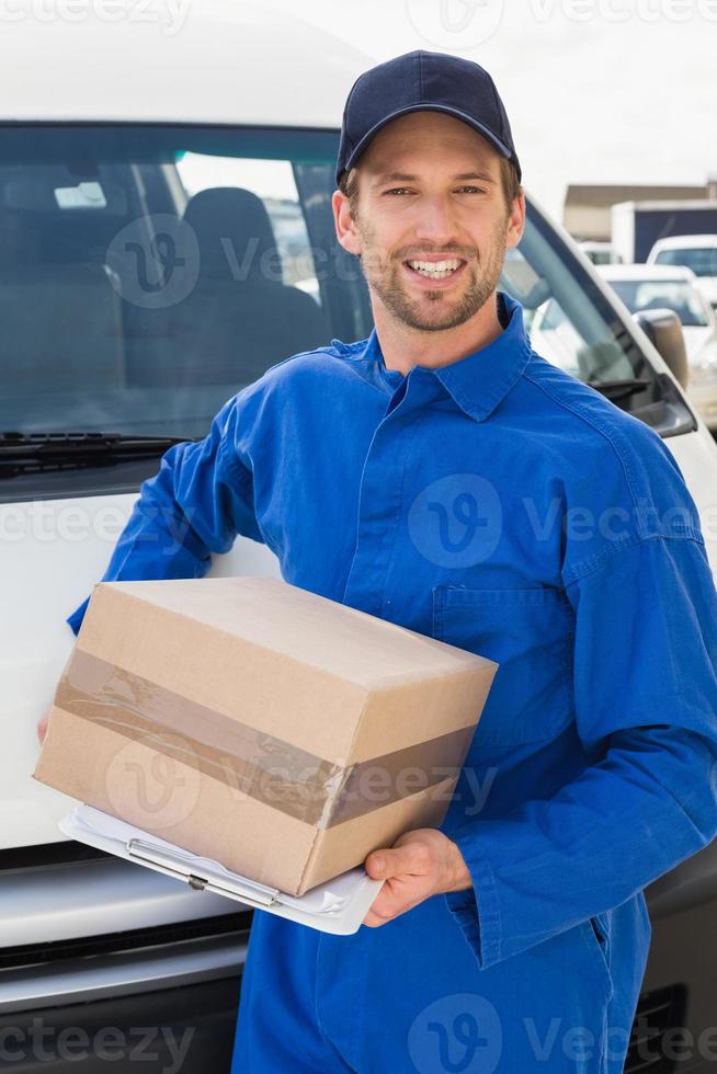motorista de entrega sorrindo para a câmera por sua van segurando a parcela foto