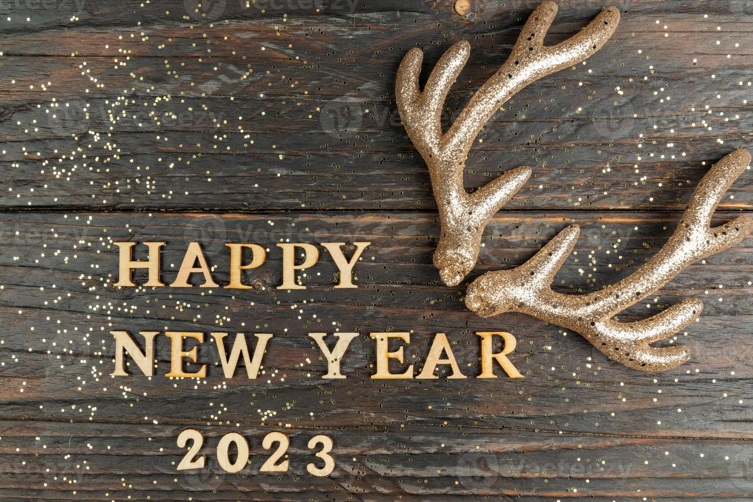 feliz ano novo 2023 letras de madeira em um fundo festivo com lantejoulas e chifres de rena de brinquedo. saudações, cartão postal. foto