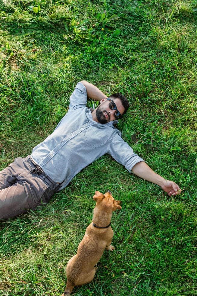 homem e cachorro deitado na grama verde no verão, vista superior. homem europeu atraente descansando com seu cachorro. foto