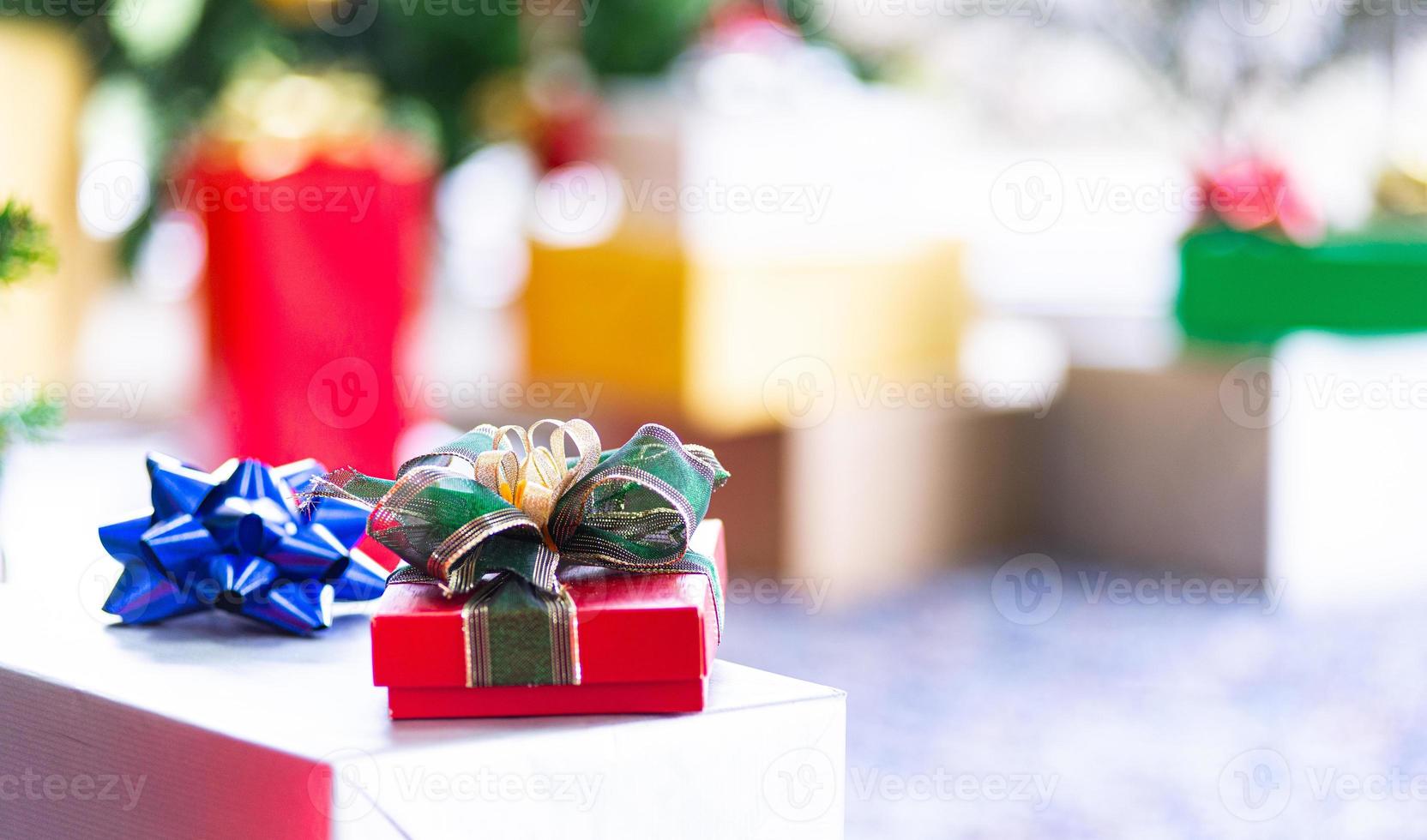 conceito de férias de natal e ano novo. closeup de caixas de presente coloridas de natal e ano novo com fita vermelha na decoração da árvore de natal com bolas de fitas e fundo de ornamentos foto