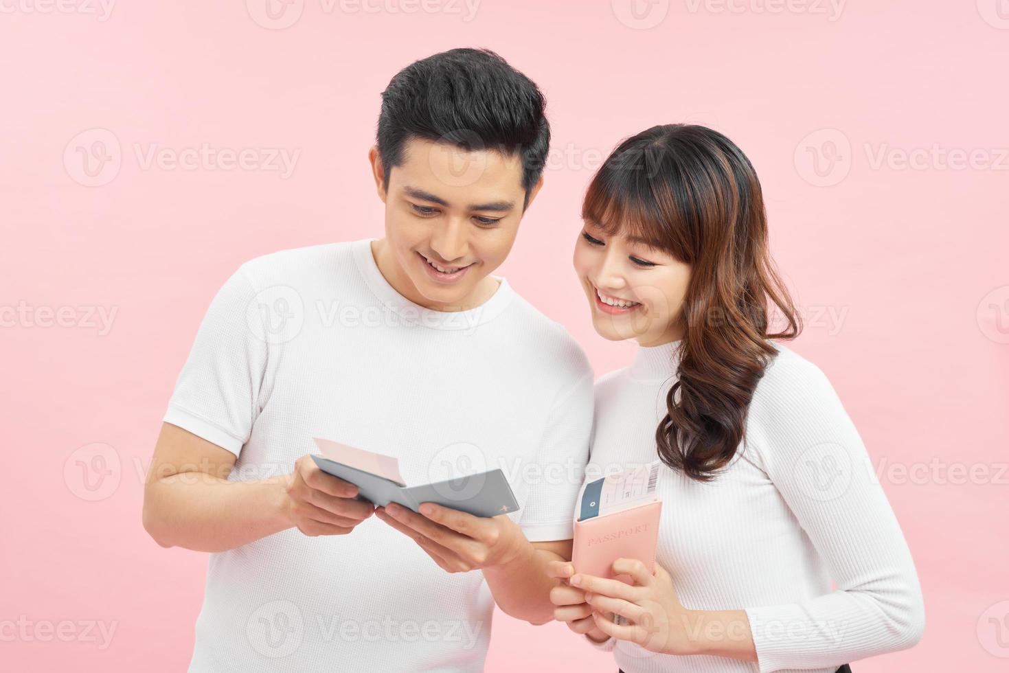 retrato de um jovem casal atraente alegre dançando isolado sobre fundo rosa, mostrando passaporte com passagens aéreas foto