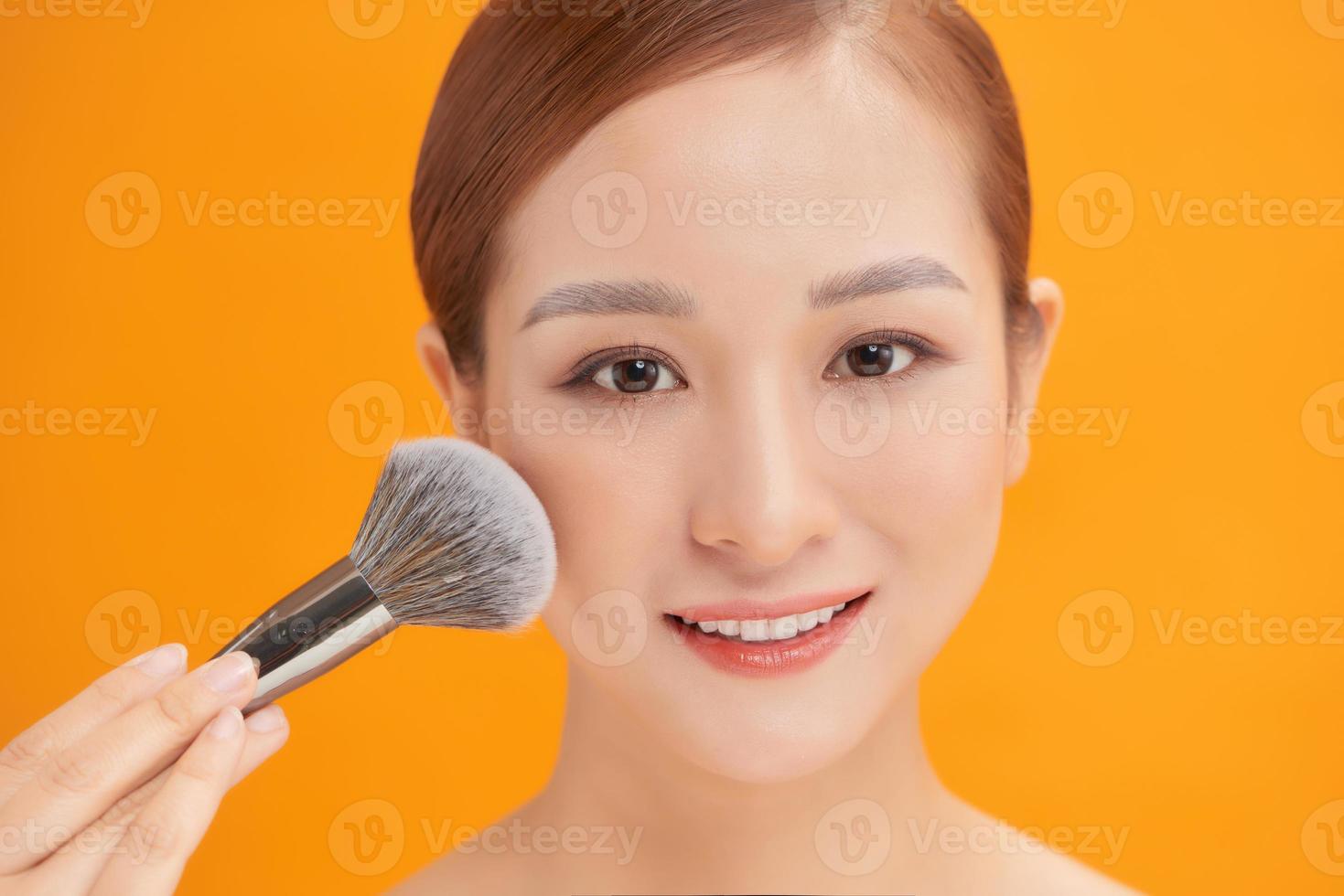 beleza. Maquiagem. mulher bonita aplicando base tonal cosmética seca no rosto usando pincel de maquiagem. foto