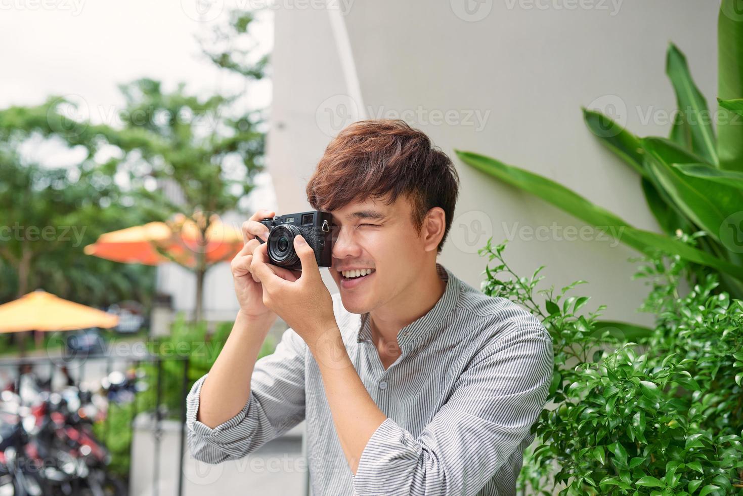sorrindo jovem macho sentado à mesa no café com câmera fotográfica enquanto bebe café foto