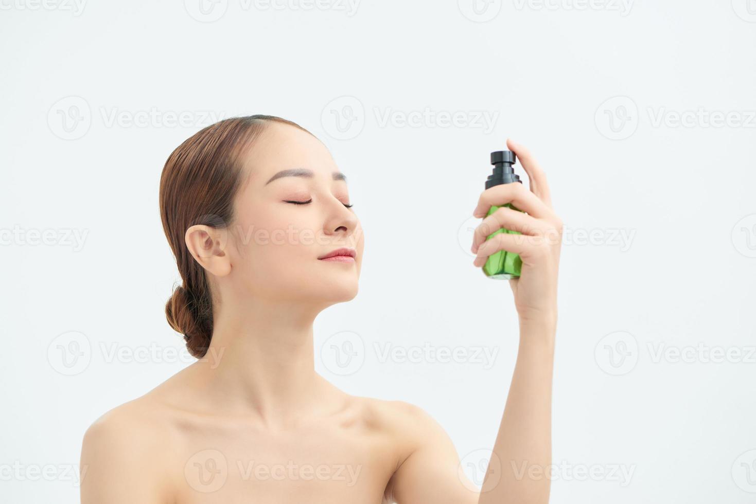 jovem mulher aplicando água termal no rosto contra um fundo branco. produto cosmético foto