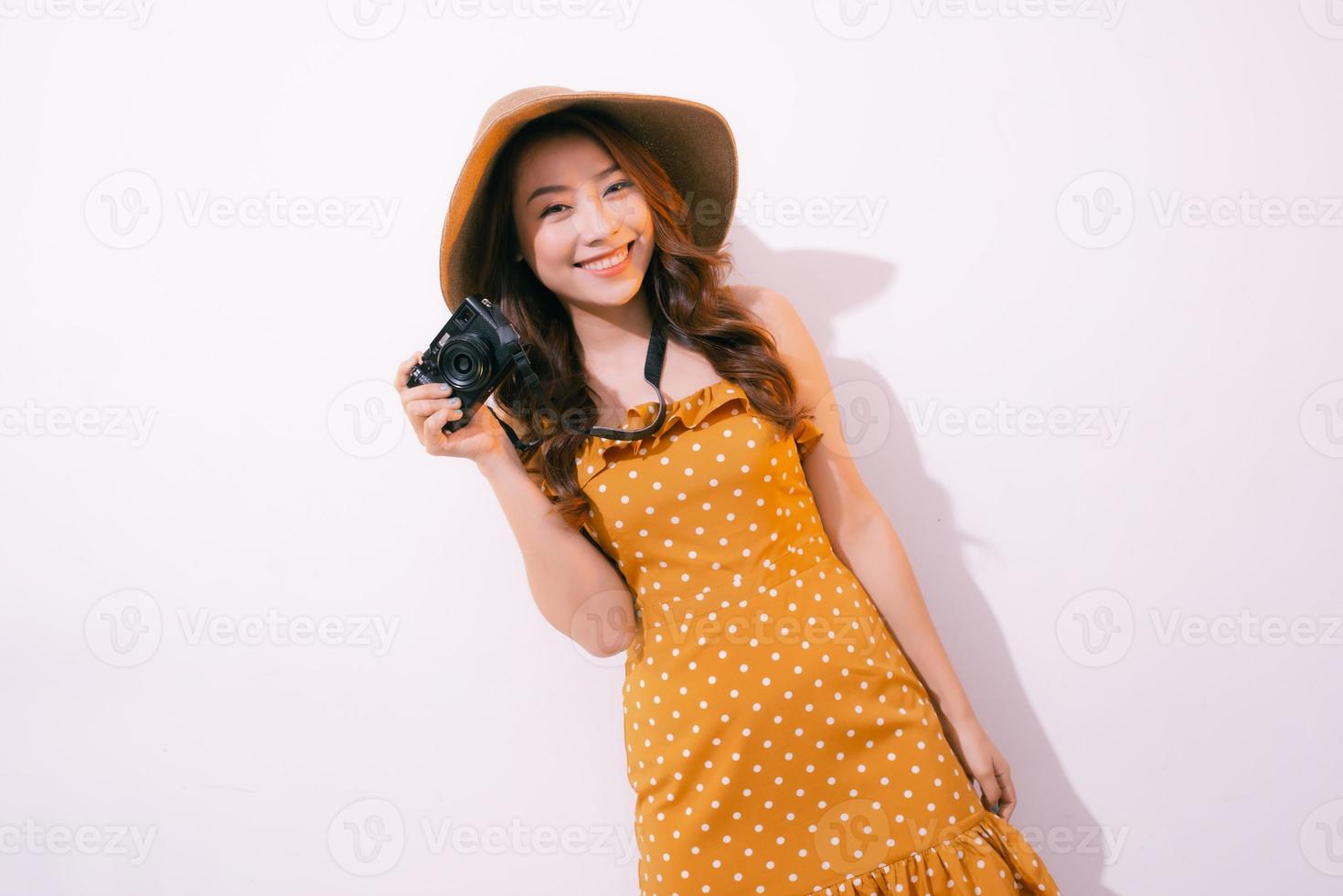 fechar o retrato de uma menina bonita sorridente no vestido tirando foto em uma câmera retro isolada sobre fundo rosa