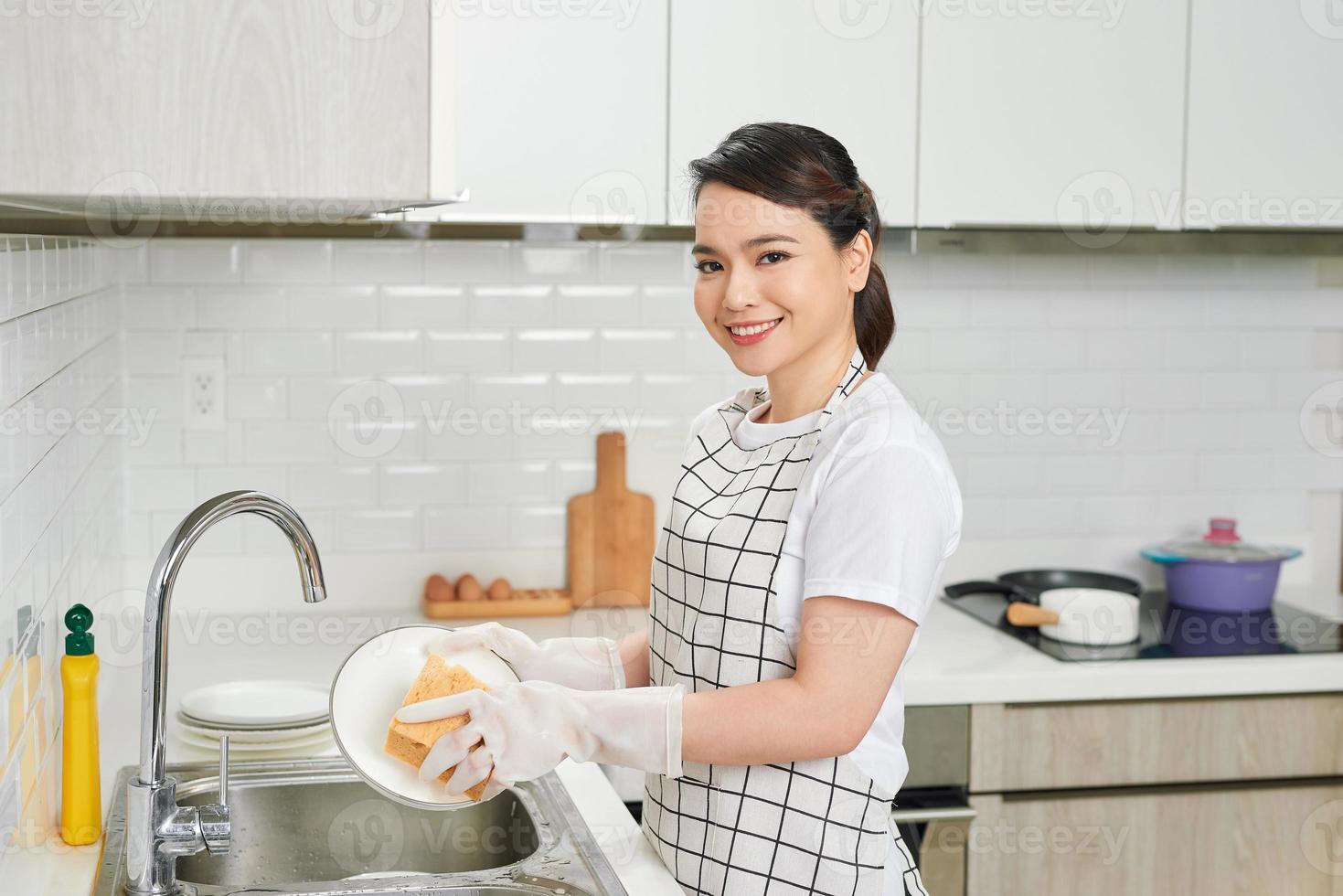 mãos de mulher jovem com bela manicure lavando pratos na pia da cozinha usando esponja com espuma de sabão foto