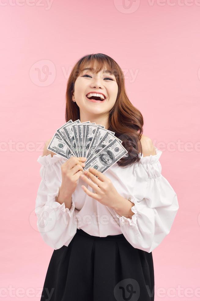 imagem de mulher encantada vestindo roupas básicas sorrindo e segurando dinheiro isolado sobre fundo rosa foto