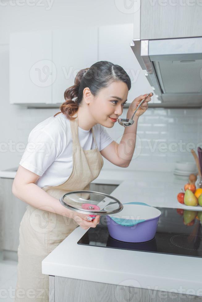 jovem mulher saboreando comida com colher na cozinha foto