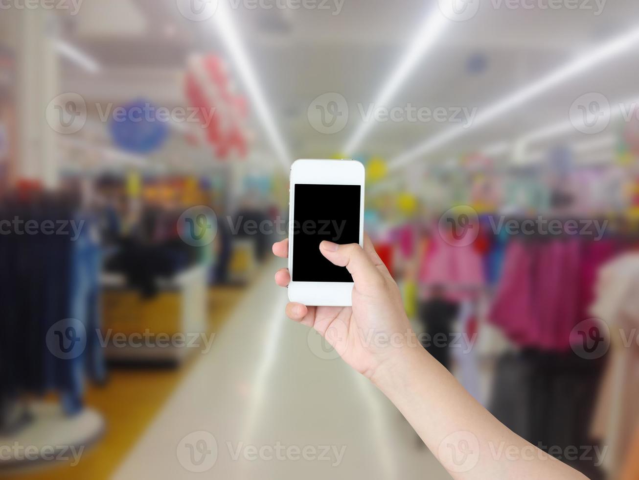 mão segurando o celular com fundo desfocado corredor de prateleiras de supermercado foto