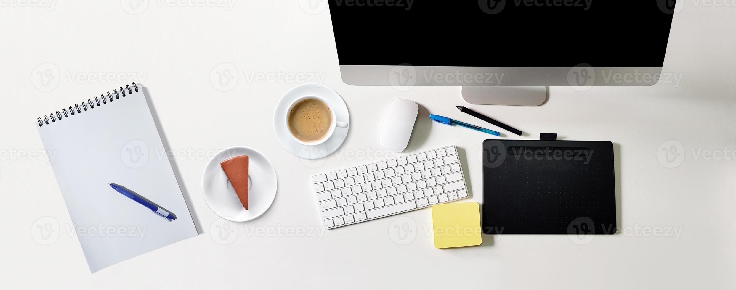 mesa branca moderna com computador de tela preta, xícara de café, bolo de chocolate. caderno para escrever mensagens, caneta, vista superior, conceito de mesa foto