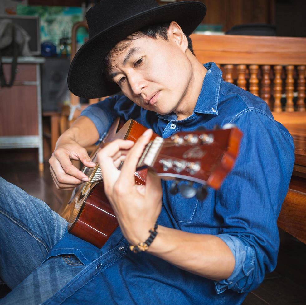 hipster de músico masculino asiático tocando violão ou praticando violão para lazer ou idéias de hobby para férias relaxantes em casa. foto