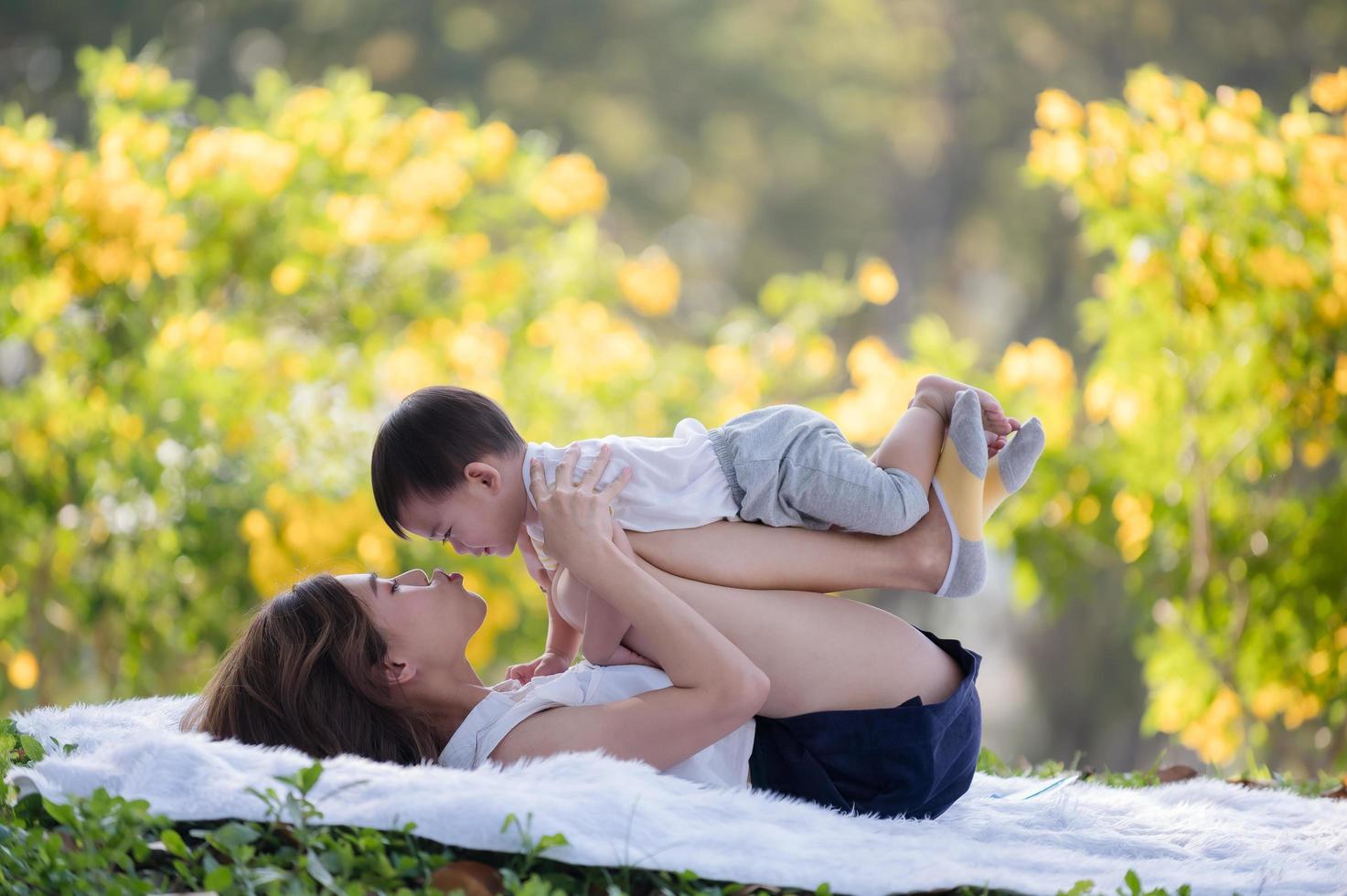 um menino asiático deita-se nas pernas de sua mãe, que são levantadas do chão de pano foto