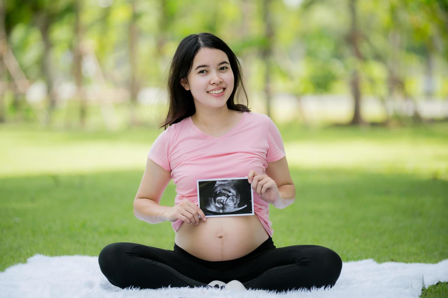 uma mulher asiática que está grávida pela primeira vez senta e relaxa para mostrar suas imagens de um ultra-som hospitalar para verificar a saúde de seu bebê em crescimento foto