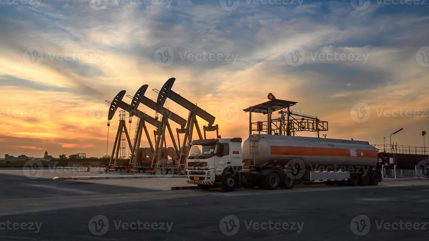 plataformas de petróleo e caminhões de petróleo estão trabalhando ou estacionados para drenar petróleo em campos de petróleo. ao pôr do sol ou nascer do sol à noite ou de manhã foto