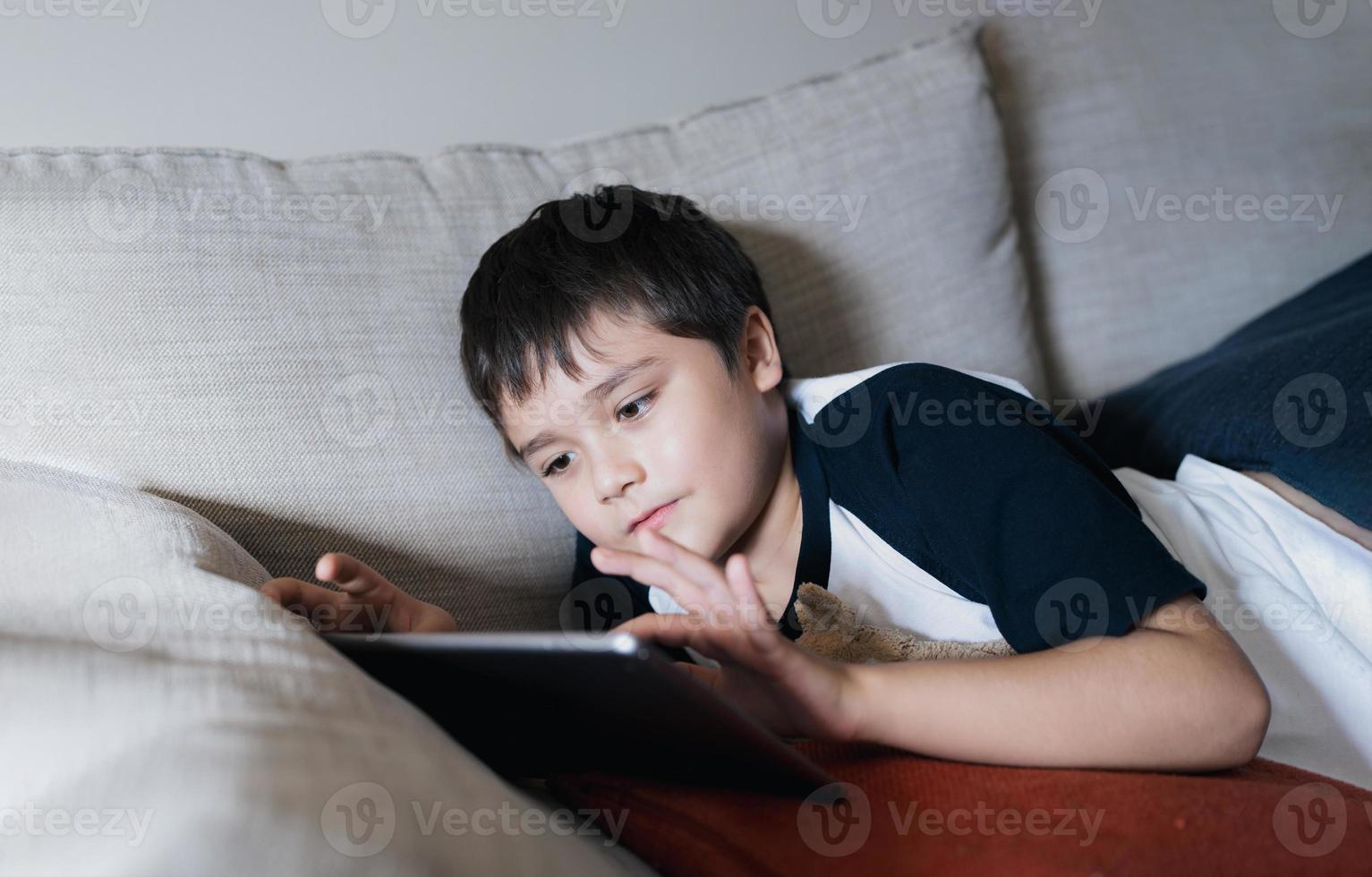 menino de escola usando tablet estudando on-line na internet, criança jogando ou assistindo desenho animado na almofada digital, criança feliz relaxando em casa, crianças com tecnologia e conceito de rede social foto