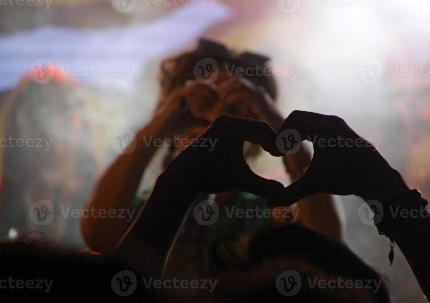 membro da platéia formando um coração com as mãos durante um show foto