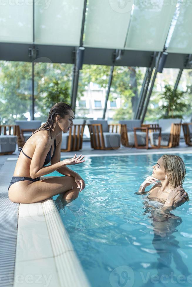 duas amigas em trajes de banho sentados à beira da piscina, aproveitando as férias de verão na piscina interior foto