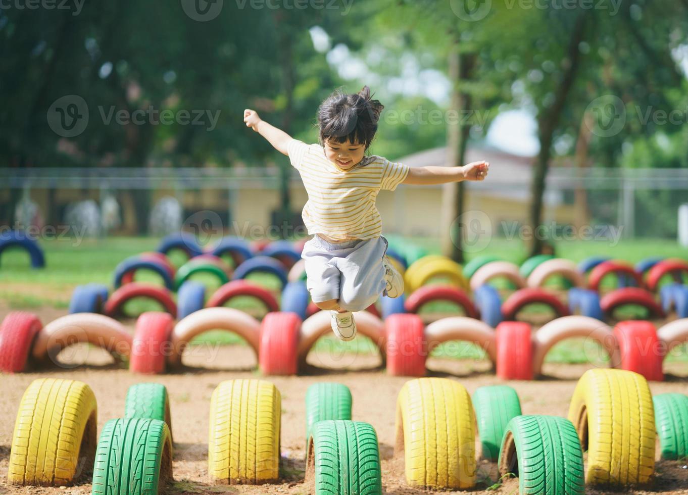 sorriso de linda garota asiática brinca pulando no jardim de infância da escola ou no playground. atividade de verão saudável para crianças. menina asiática escalando ao ar livre no playground. criança brincando no playground. foto