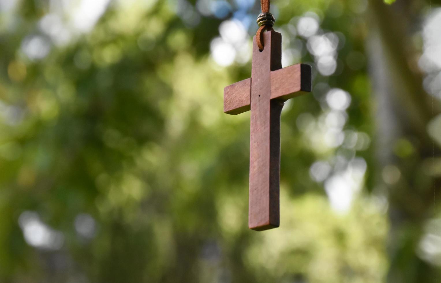 cruz de madeira pendurada no galho de árvore, foco suave e seletivo, fundo de árvore bokeh natural, conceito de esperança, amor, perdão e crença em jesus ao redor do mundo. foto