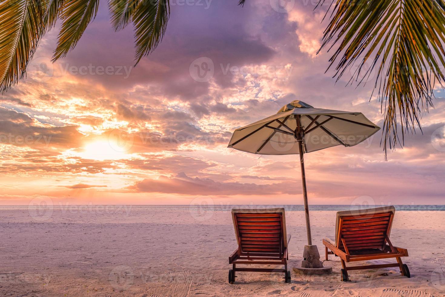 cenário perfeito do pôr do sol tropical, duas espreguiçadeiras, espreguiçadeiras, guarda-chuva sob palmeira. areia branca, vista para o mar com horizonte, céu crepuscular colorido, calma e relaxamento. hotel resort de praia inspirador foto