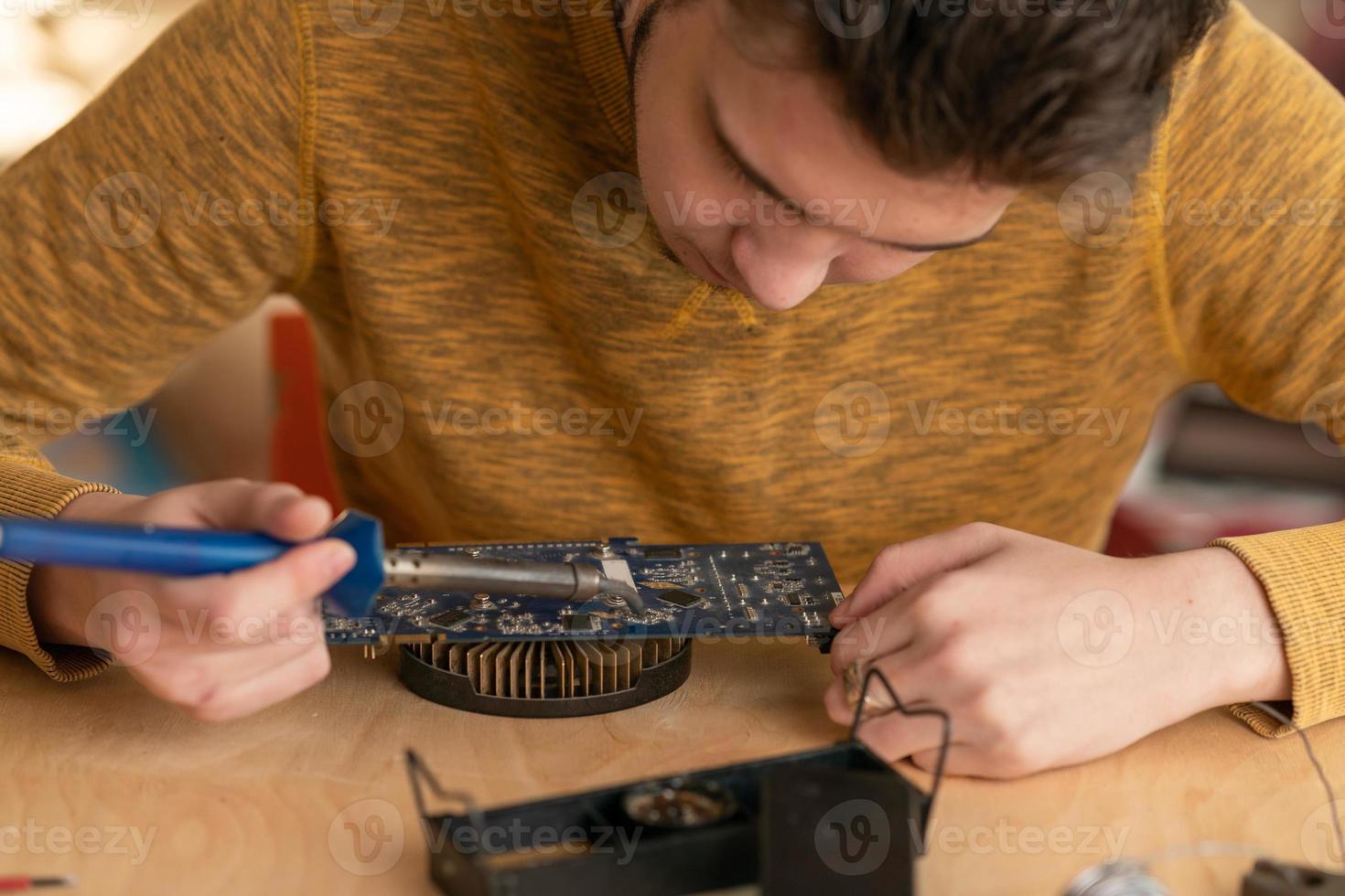 um jovem solda um microcircuito queimado com um ferro de solda foto