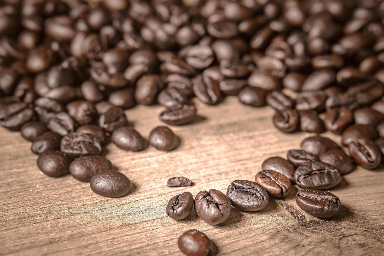 café em fundo de madeira. grãos de café torrados marrons, sementes em fundo escuro. expresso escuro, aroma, bebida de cafeína preta. closeup isolado energia mocha, ingrediente cappuccino. foto