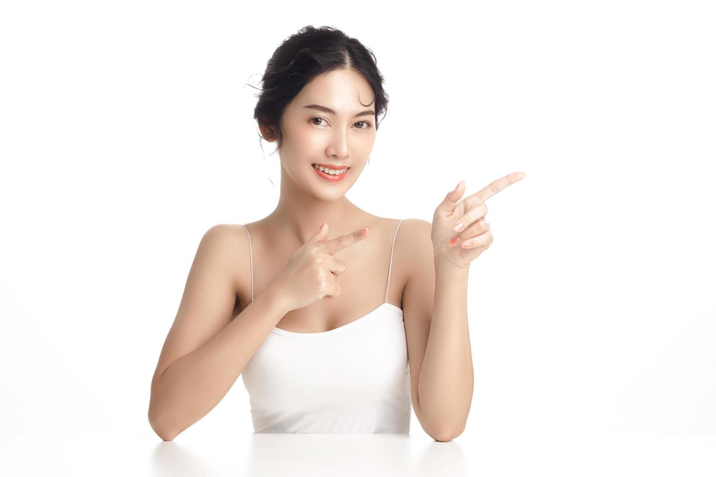 mulher asiática com um rosto bonito e pele fresca limpa perfeita. modelo feminino bonito aponta no espaço livre no fundo branco isolado. tratamento facial, cosmetologia, conceito de beleza. foto