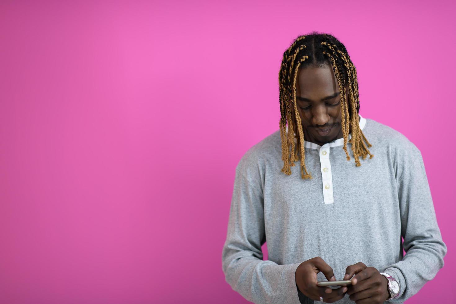 cara afro usa um telefone enquanto posava na frente de um fundo rosa. foto