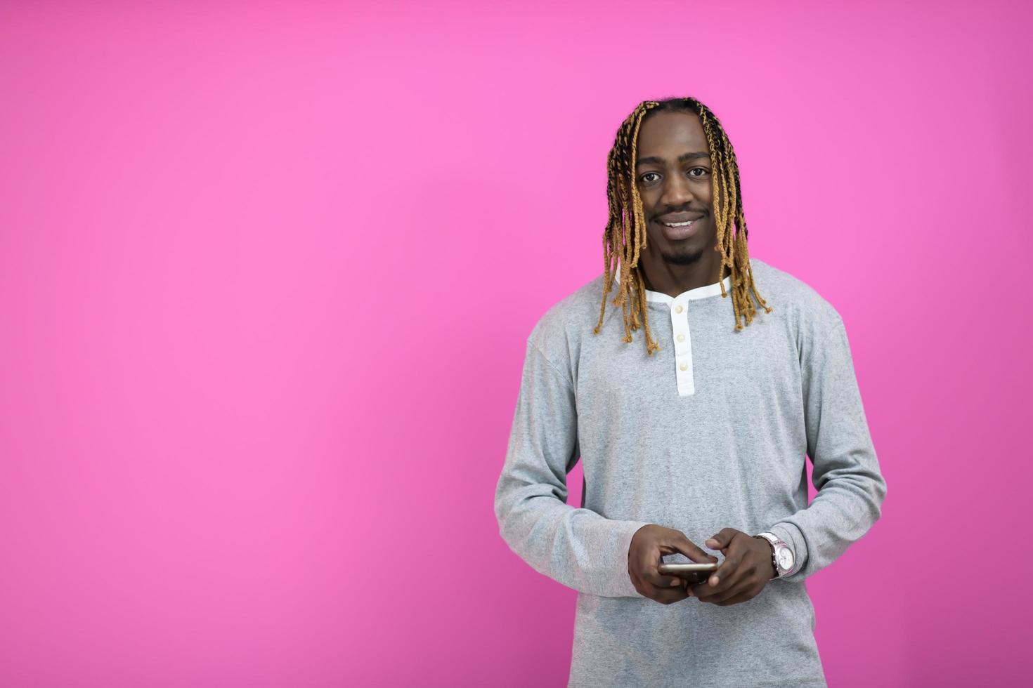 cara afro usa um telefone enquanto posava na frente de um fundo rosa. foto