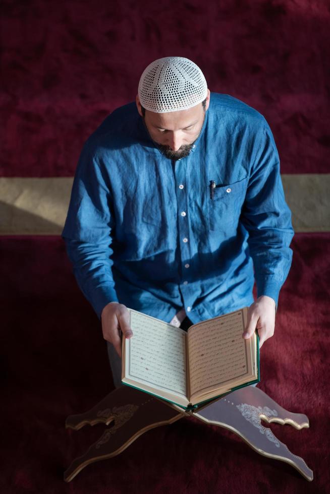 homem muçulmano rezando sozinho a Deus dentro da mesquita e lendo o livro islâmico de azevinho foto