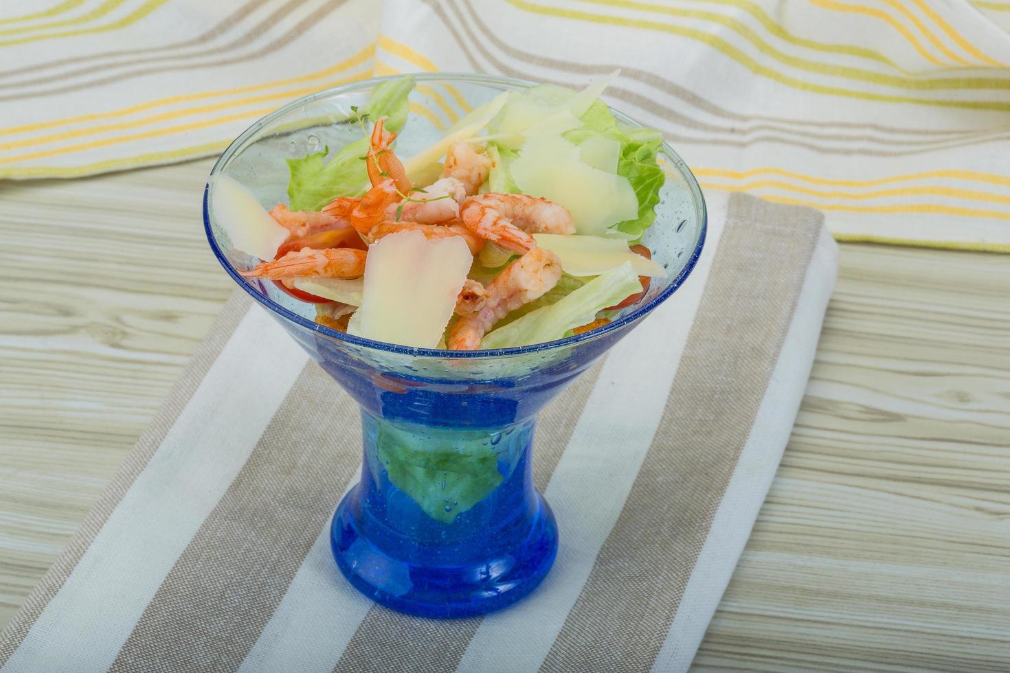 salada caesar com camarões em uma tigela sobre fundo de madeira foto