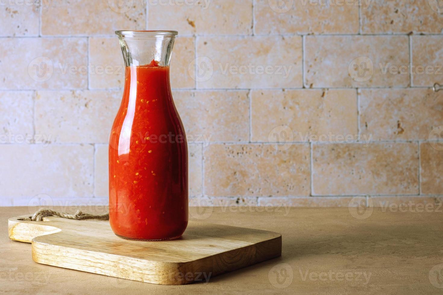 uma garrafa de vidro com molho de tomate caseiro fica em uma tábua de madeira foto