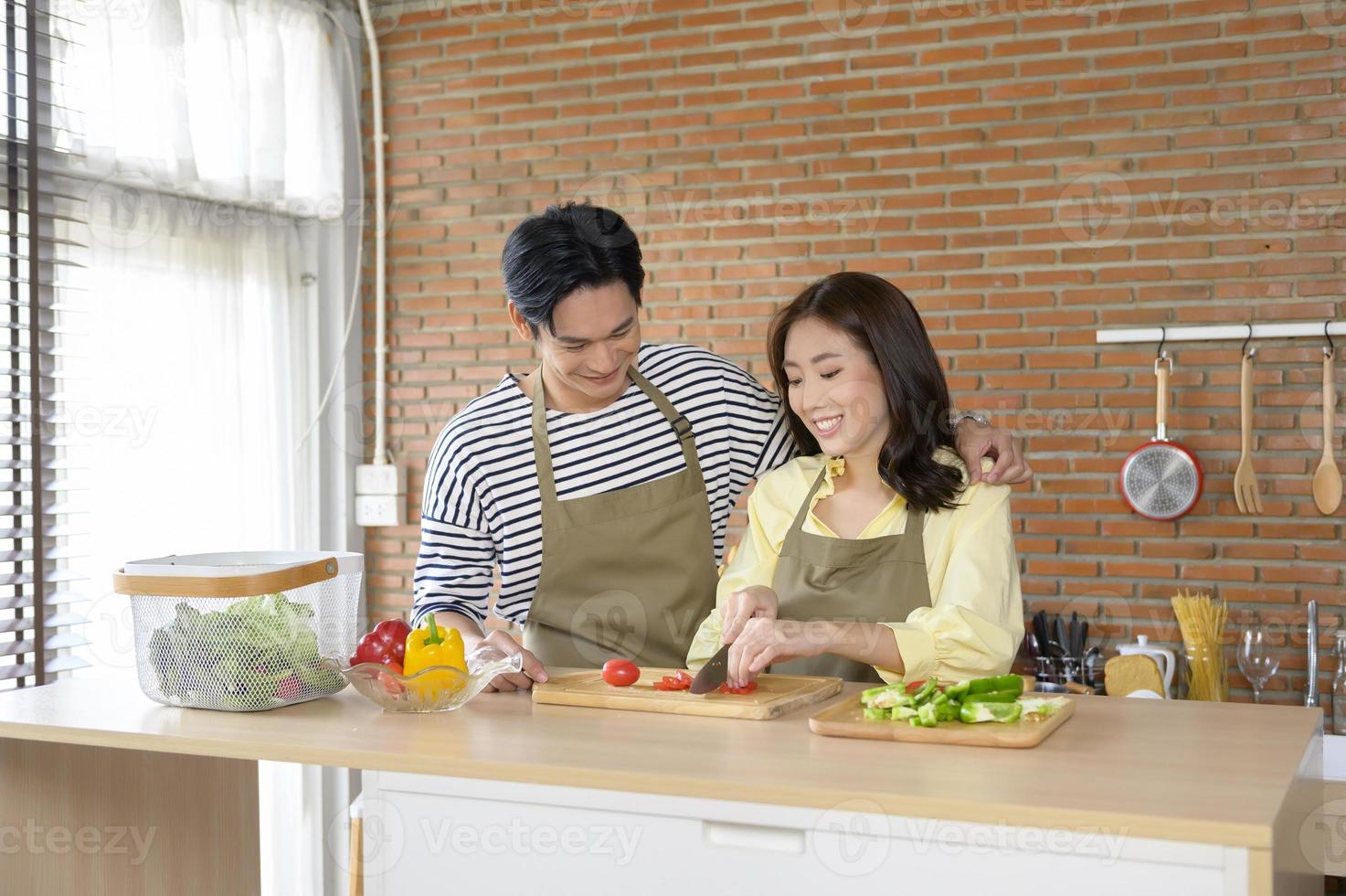 jovem casal asiático sorridente vestindo um avental na sala da cozinha, cozinhando o conceito foto