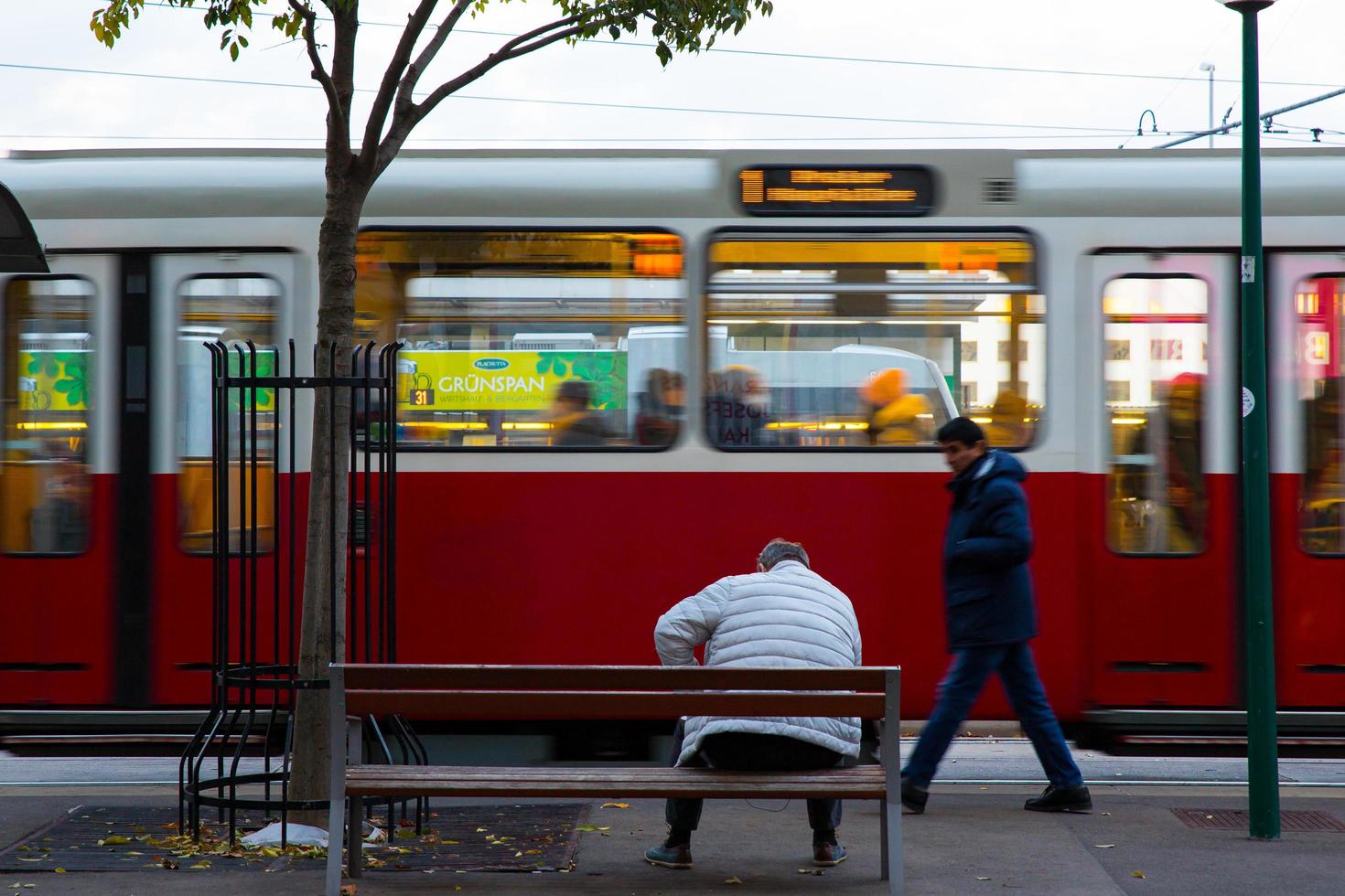 viena, áustria, 2021 - cena urbana de um homem maduro sentado em um banco esperando o transporte público tradicional em viena, o bonde elétrico, áustria foto