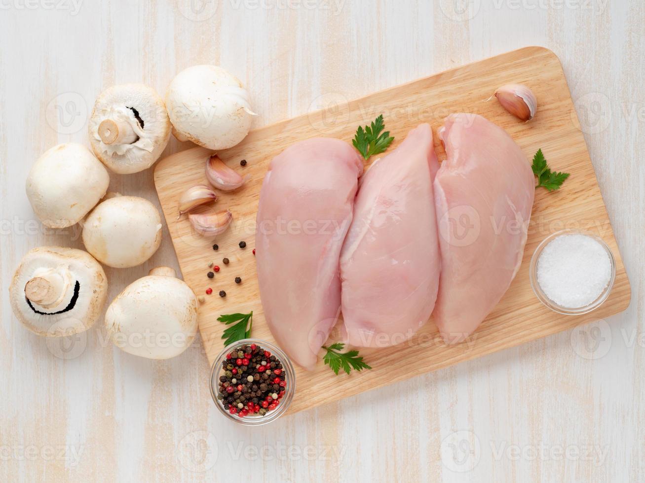 filé de peito de frango cru com especiarias na placa de madeira na mesa de madeira branca foto