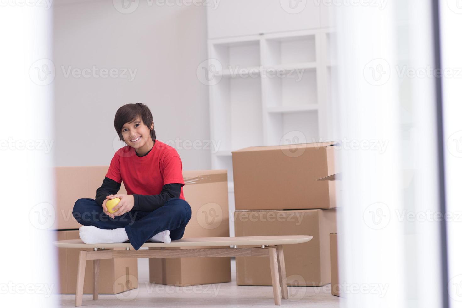 menino sentado na mesa com caixas de papelão ao redor dele foto